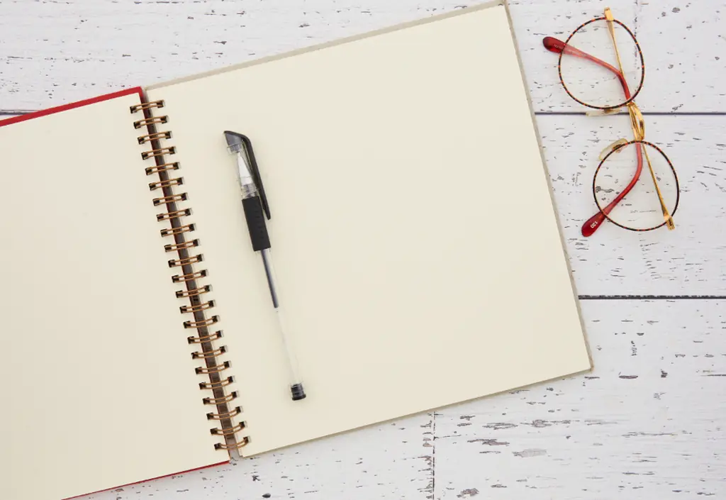 Une table claire, avec lunettes, stylo et carnet posé ouvert